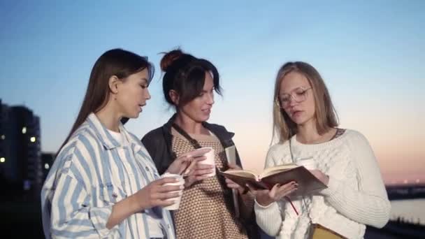 Tres mujeres jóvenes tomando café y leyendo un libro . — Vídeos de Stock