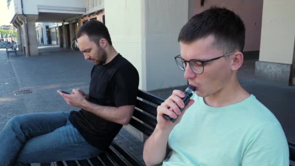 Man in glasses smoking vape and disturbing another man with a smoke. — Stock Video