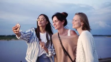 Üç kadın model selfie çekiyor ve yürürken telefondaki fotoğraflara bakıyor.