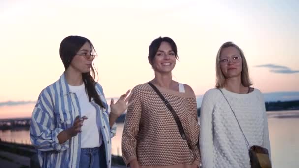 Three women talking and laughing outside in sunset. — Stock Video