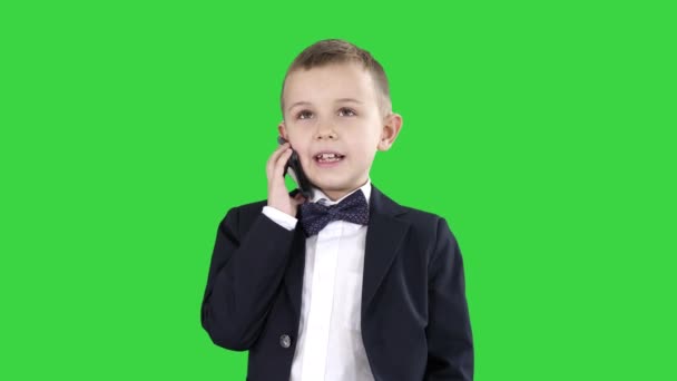 Schattige kleine jongen praten op zijn smartphone en staan in een donker pak op een groen scherm, Chroma Key. — Stockvideo