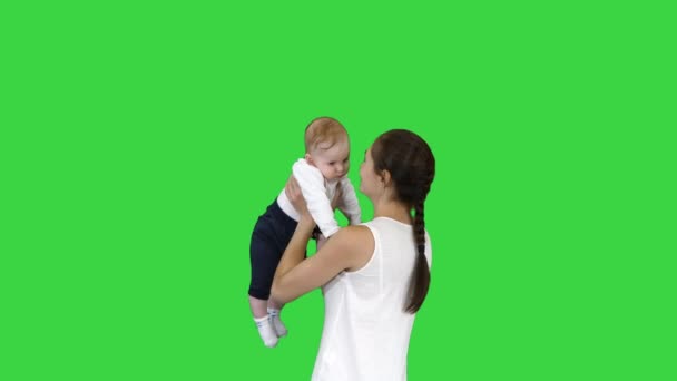 Young mama playing with baby by rising him up on a Green Screen, Chroma Key. — Stock Video