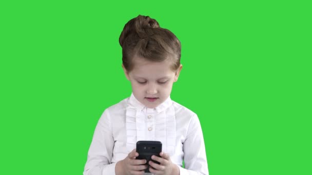 Söt liten flicka ser ut i smartphone och skriva ett meddelande på en grön skärm, Chroma nyckel. — Stockvideo