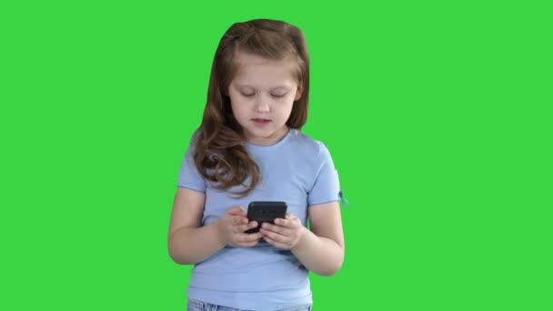 Pequena menina bonito surpreso com uma informação interessante no smartphone móvel em uma tela verde, Chroma Key . — Vídeo de Stock