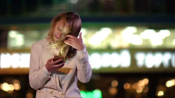 Mulher bonita usando seu telefone tarde da noite, quando as luzes estão se desligando no edifício atrás dela . — Vídeo de Stock