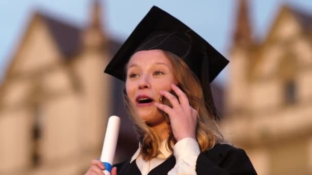 Gecelikle mezun olup cep telefonuyla konuşan mutlu bir kız.. — Stok video