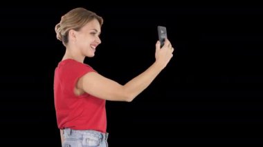 Güzel genç kadın yürüyüş ve fotoğraf ve selfie çekmek için bir akıllı telefon tutarak, Alpha Channel