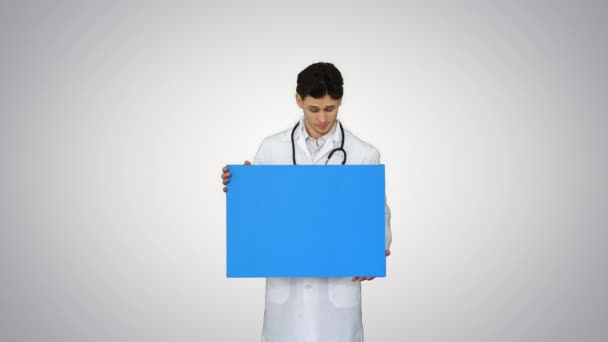 Médecin souriant portant un stéthoscope tenant une affiche vierge sur fond de dégradé . — Video