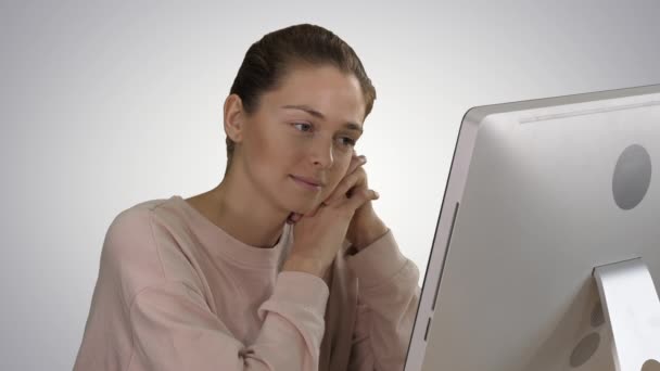 グラデーションの背景にビデオを見てコンピュータのモニターを見てピンクのプルオーバーを持つブロンドの女の子. — ストック動画