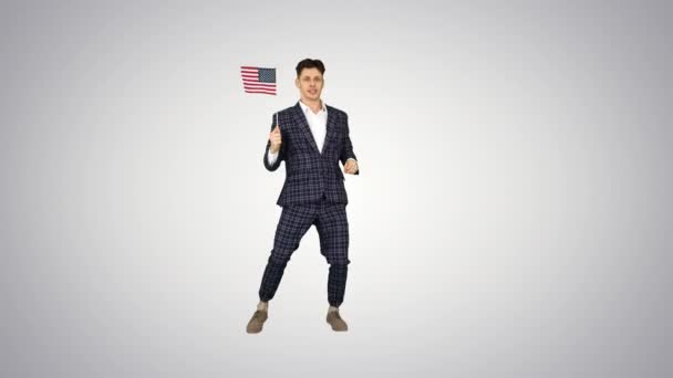 Fajny człowiek w garniturze robi szalony taniec z amerykańską flagą na tle gradientu. — Wideo stockowe