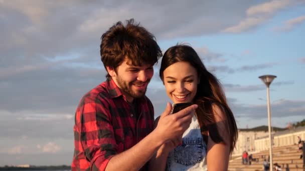 Couple heureux regardant des photos dans un téléphone intelligent à l'extérieur. — Video