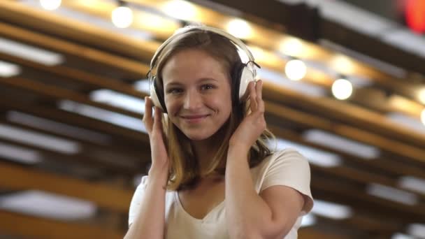 カメラを見て笑顔でヘッドフォンで音楽を聴く美しい魅力的な若い女性. — ストック動画