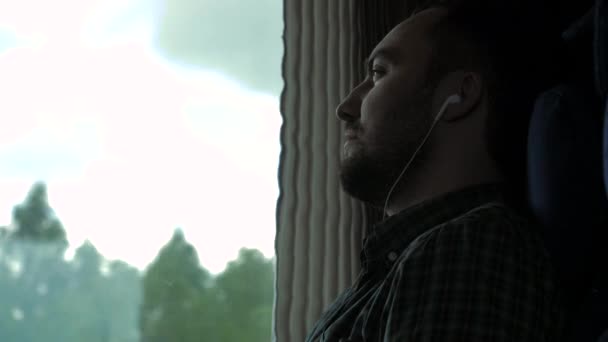 Vážný muž u okna ve vlaku, poslouchající hudbu. — Stock video