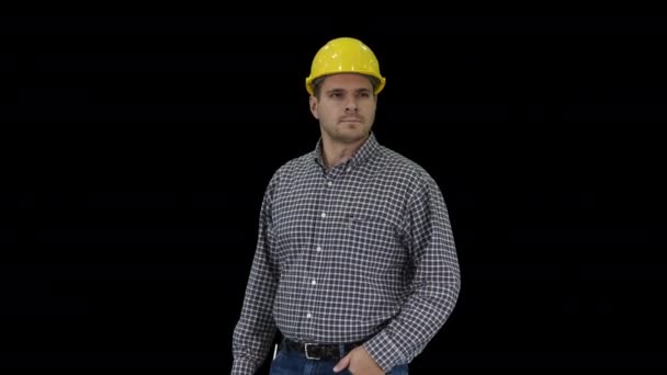 完璧なよく構築されたオブジェクトを見て黄色のヘルメットに笑みを浮かべて建設労働者腰の手、アルファチャンネル — ストック動画