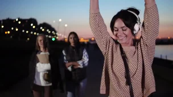 幸せな若い女性は、ウォーターフロントを歩きながら笑顔でヘッドフォンを介して音楽を聴きます. — ストック動画
