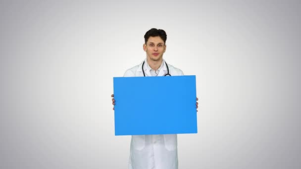 Feliz sonriente médico masculino mostrando letrero en blanco y bailando sobre fondo degradado. — Vídeos de Stock