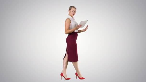 Woman walking using digital tablet and talking to camera on gradient background. — Stock Video