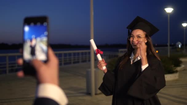 Sonriente estudiante graduada femenina es fotografiada por su amiga. — Vídeo de stock