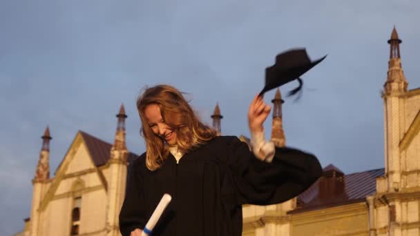 Graduación - chica lanza su sombrero en el aire y sonríe a la cámara en un día soleado brillante . — Vídeos de Stock