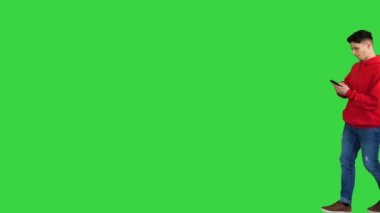Yakışıklı, sıradan bir adam, akıllı telefonuyla müzik dinliyor ve yeşil ekranda yürürken dans ediyor, Chroma Key.