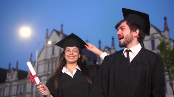 Heureux jeunes diplômés dansant et célébrant la remise des diplômes dans le parc près de l'académie. — Video
