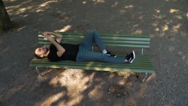 Handsome man lying on the bench outdoors and using smartphone. — Stock Video