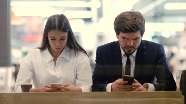 Hombre y mujer sentados en el café del centro comercial usando sus teléfonos inteligentes. Gadget adicto . — Vídeos de Stock