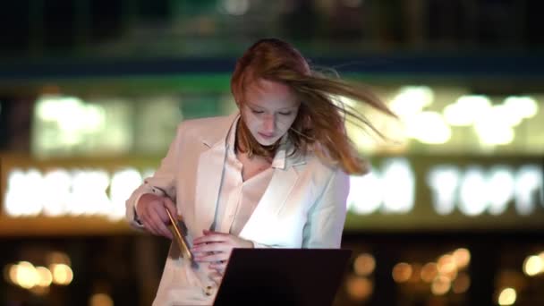 Jonge mooie vrouw met smartphone zittend met laptop buiten in de avond. — Stockvideo