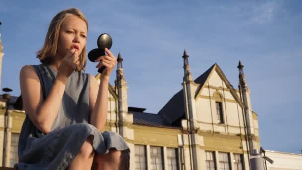 Chica bonita aplicando maquillaje mientras está sentado al aire libre cerca de la universidad . — Vídeos de Stock