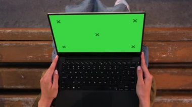 Bankta oturan bir kadın dizüstü bilgisayara bakıyor..