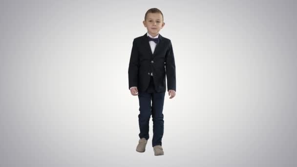 Kleine jongen in een kostuum met een vlinderdas wandelen op gradiënt achtergrond. — Stockvideo