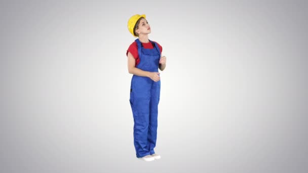Женщина-инженер в жёлтом шлеме, глядя вверх, поражена зданием, статистикой или графиком на градиентном фоне . — стоковое видео