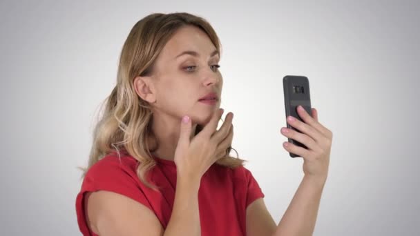Όμορφη γυναίκα καμάρωμα χρησιμοποιώντας το τηλέφωνό της σαν καθρέφτης στο φόντο ντεγκραντέ. — Αρχείο Βίντεο