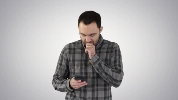 Sad young man walking and looking at his mobile phone with his hand on his face on gradient background. — Stock Video