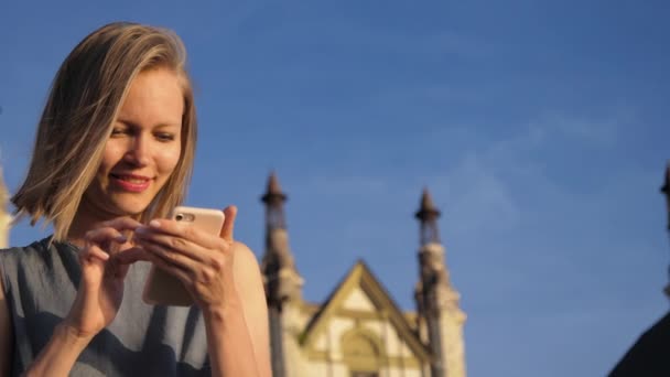 미소와 함께 건물 근처에 앉아 스마트 폰을 사용하여 아름다운 유행 럭셔리 여자. — 비디오