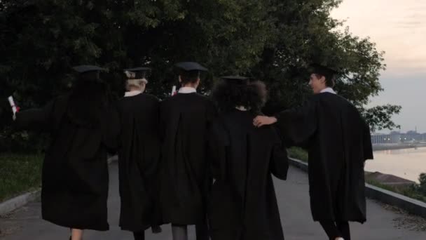 Cinco jóvenes graduados saltan mientras caminan . — Vídeos de Stock