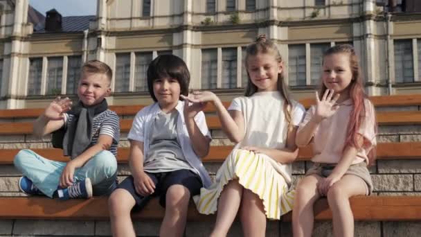 Děti s úsměvem a máváním rukama se dívají na kameru. — Stock video