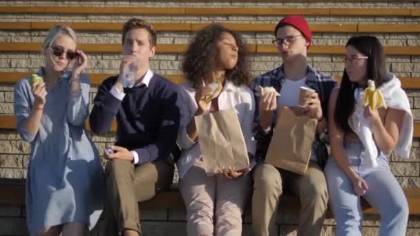 Gruppe hungriger Studenten sitzt beim Mittagessen auf der Treppe. — Stockvideo