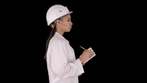 Femme ingénieur avec casque tient stylo et check-list mettre quelque chose vers le bas tout en marchant, Canal Alpha — Video