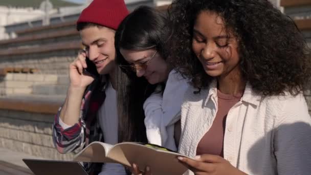 Adolescentes ao ar livre fazendo lição de casa e rindo. O rapaz está a fazer uma chamada. . — Vídeo de Stock