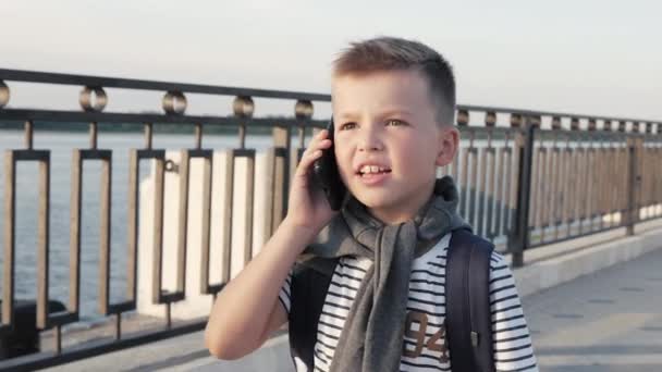 Jonge schooljongen wandelen en praten op een smartphone. — Stockvideo