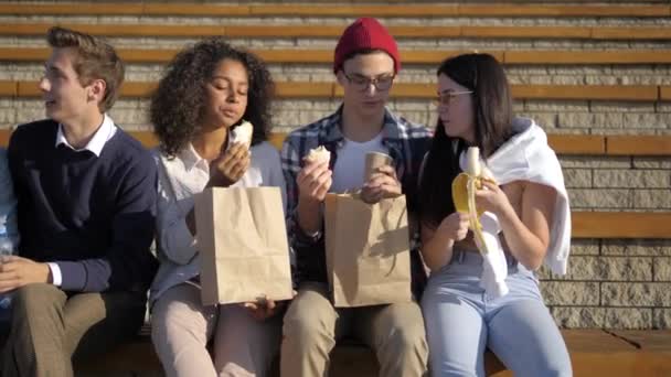 Ryhmä opiskelijoita istuu kampuksella ja syö . — kuvapankkivideo