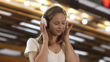 Kulaklıkla müzik dinleyen genç bir kız kameraya bakıp gülümsüyor..