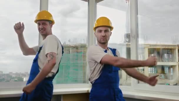 Trabajadores de Constructiona en cascos de baile cómico mirando a cámara. — Vídeos de Stock