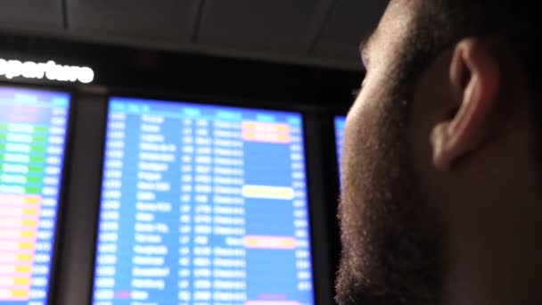 Joven hombre de negocios mirando a la junta con horario de vuelo en el aeropuerto . — Vídeo de stock