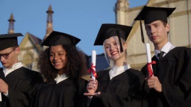 Diplomalarını göstermek için kameraya poz veren mezun öğrenciler..