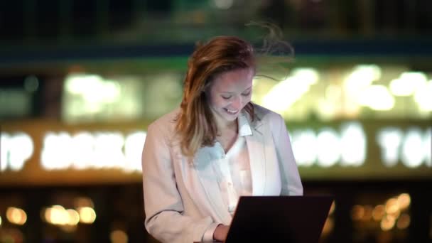 Chica encantadora freelancer sentado en el banco al aire libre en la noche, trabajando en el ordenador portátil,. Clima ventoso . — Vídeo de stock
