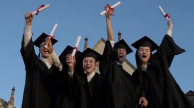 Sonunda özgür. Mezuniyet önlükleri ve üstat şapkaları giyen bir grup neşeli öğrenci mezuniyetten sonra diplomalarını tutarak bir arada duruyor.