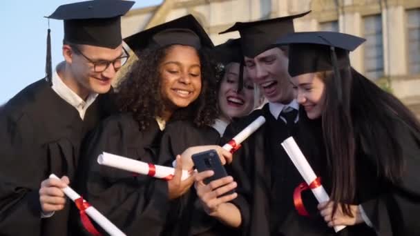 Happy group of students on graduation day laughing at something on mobile phone. — Stockvideo