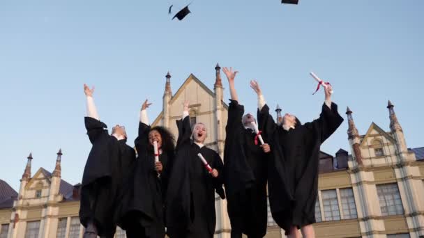 Καπέλα αποφοίτησης πετιούνται στον αέρα από μια χαρούμενη ομάδα φίλων μαθητών. — Αρχείο Βίντεο